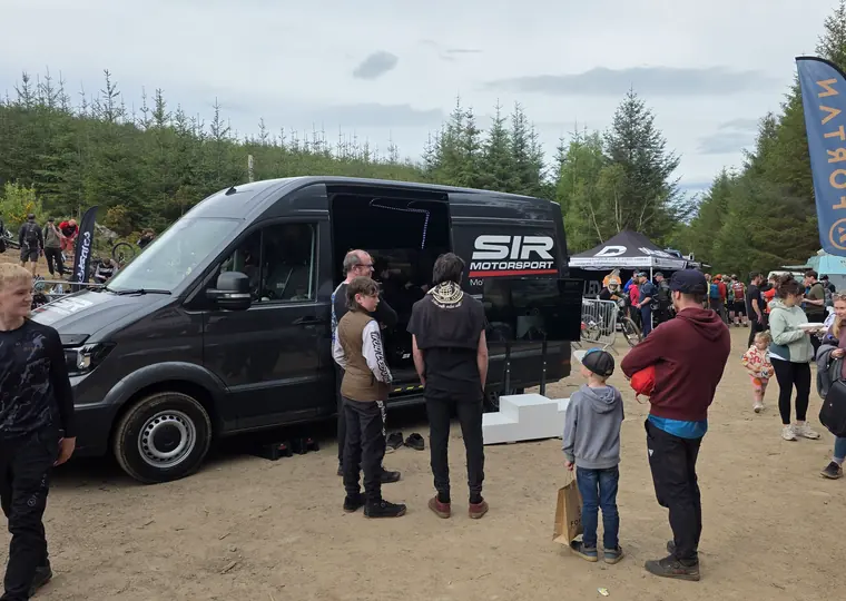 Wide shot of the SIR Motorsport van positioned within a busy outdoor event village.