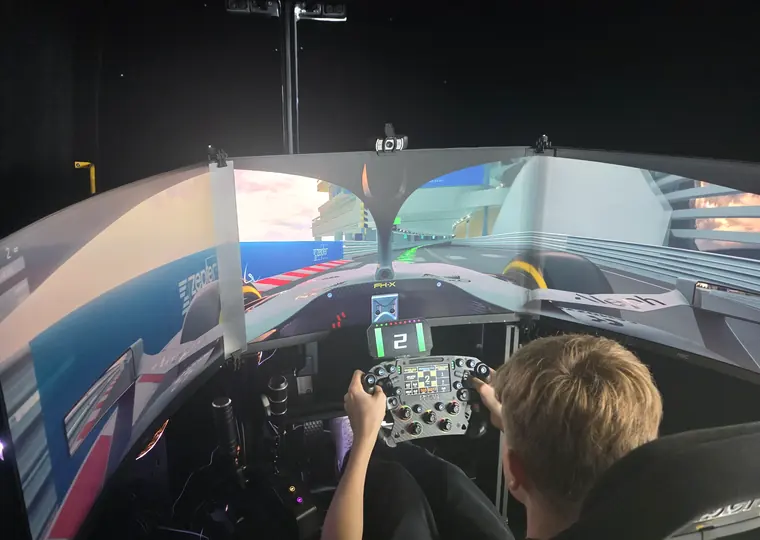 Driver using the SIR Motorsport racing simulator with triple-screen immersion.